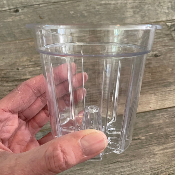 a small clear plastic flower pot being held in a hand with a wooden background