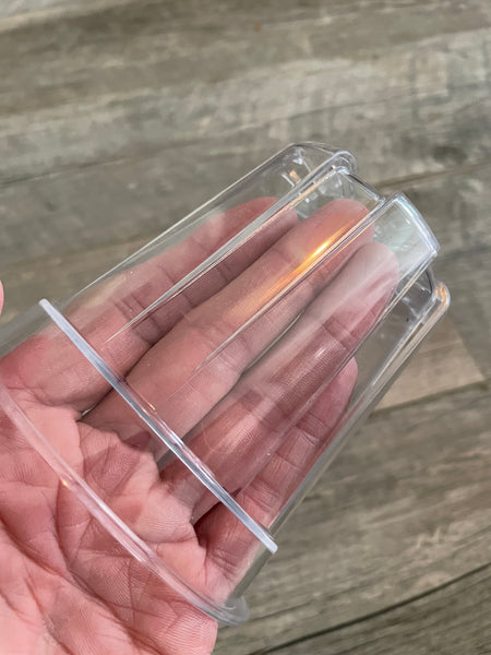 a hand holding a small clear plastic flower pot with a wooden back ground