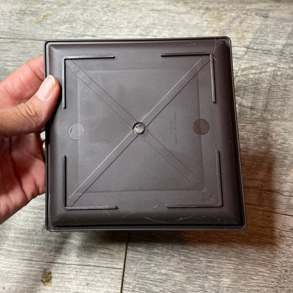 a hand holding a square brown drip tray showing the bottom of the tray